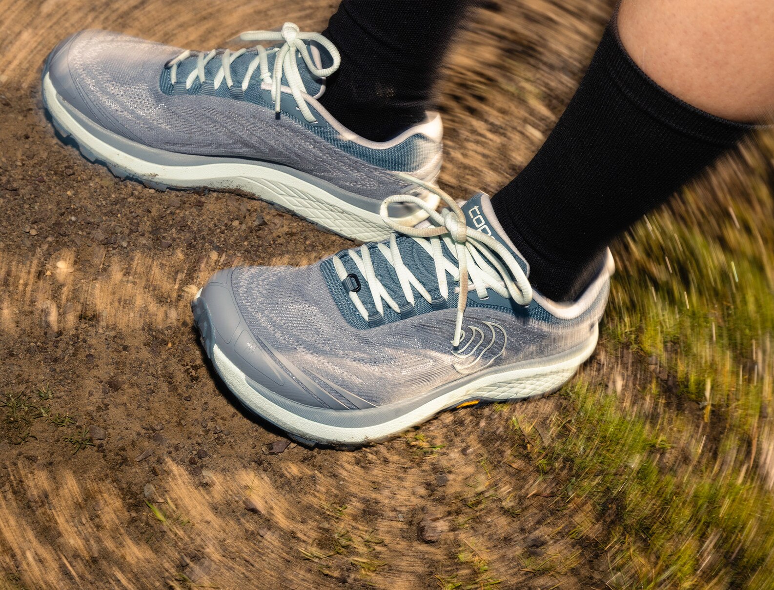 Light blue running shoes on a dirt trail, featuring motion blur to emphasize speed, paired with black socks